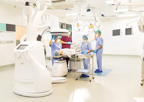 Wide angle view of a team of doctors preparing a patient for a cardiac procedure in a state of the art operating room. Endovascular equipment shown